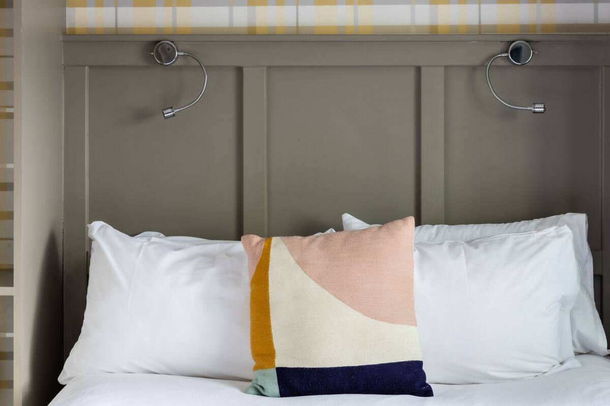 A bed with white pillows and a multicolored throw blanket.