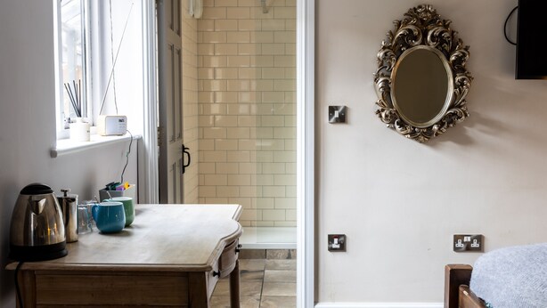 A room with a wooden table, a kettle, a blue mug, a mirror, and a tiled wall. - The Crown & Horns (Newbury)