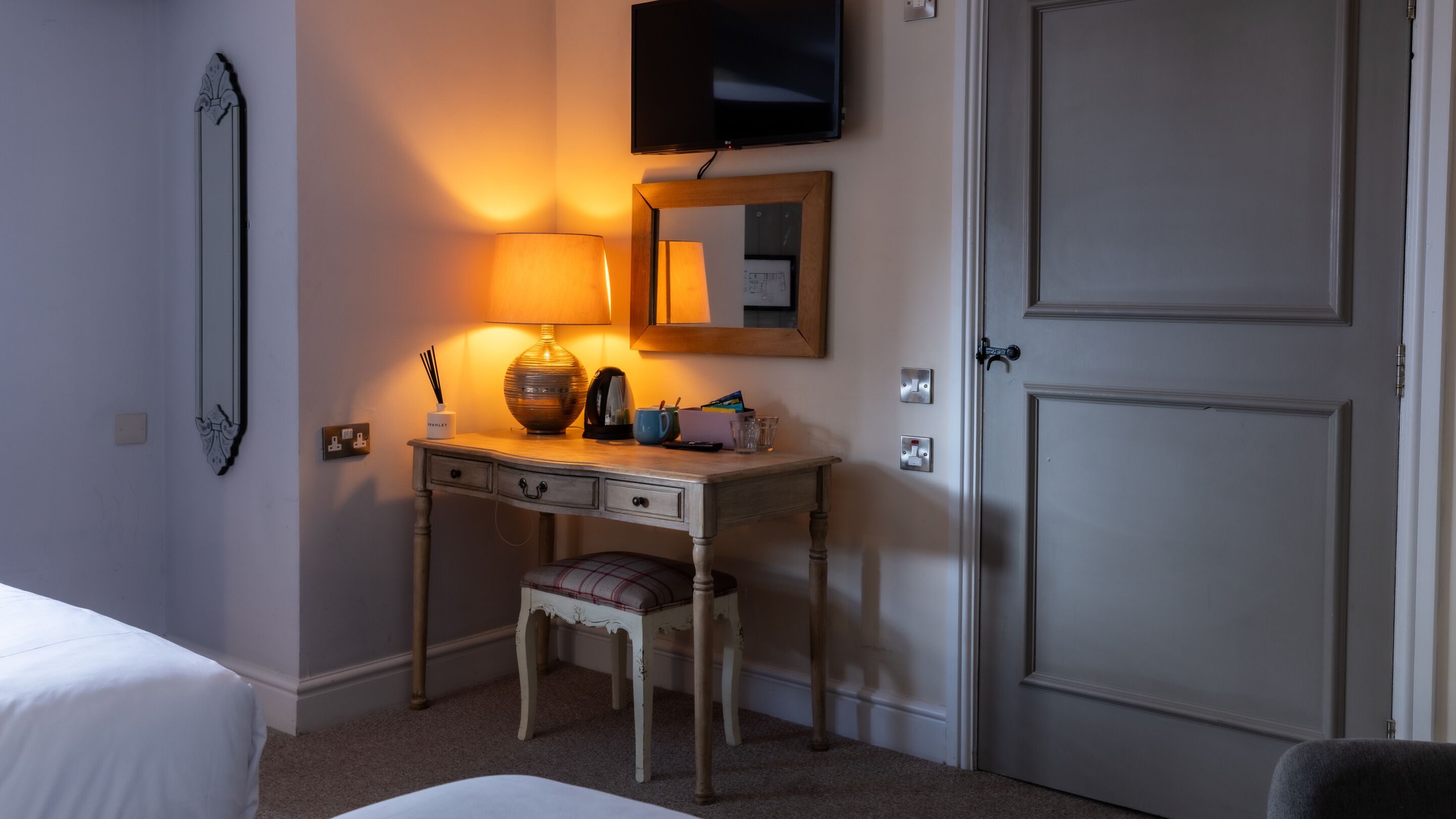 Una habitación de hotel con una cama, un escritorio con lámpara, un televisor y una puerta.