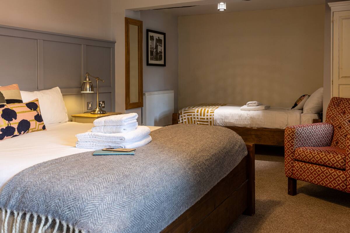 A hotel room with a large bed, a smaller bed, a chair, and a nightstand with a lamp.
