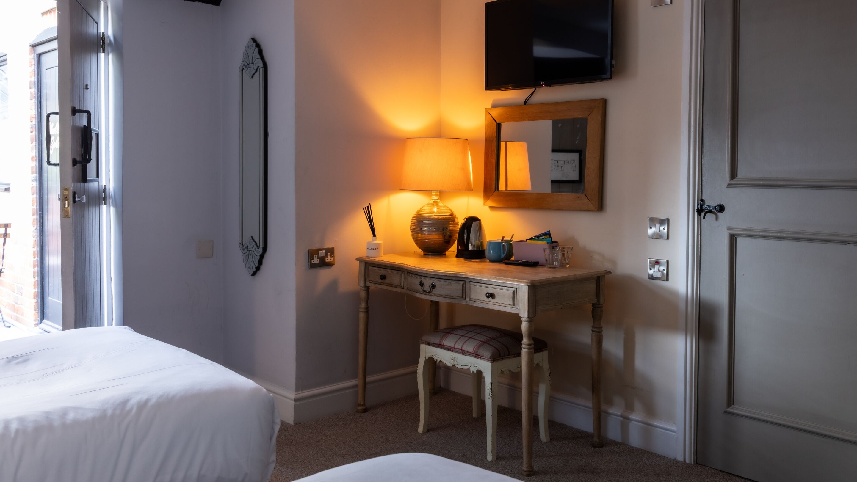 Un dormitorio con una cama, un escritorio con lámpara, un televisor y un espejo.