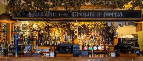 Un bar con un cartel que dice 'Welcome to the Croft & Horns', varias botellas de licores y una grifo de cerveza.