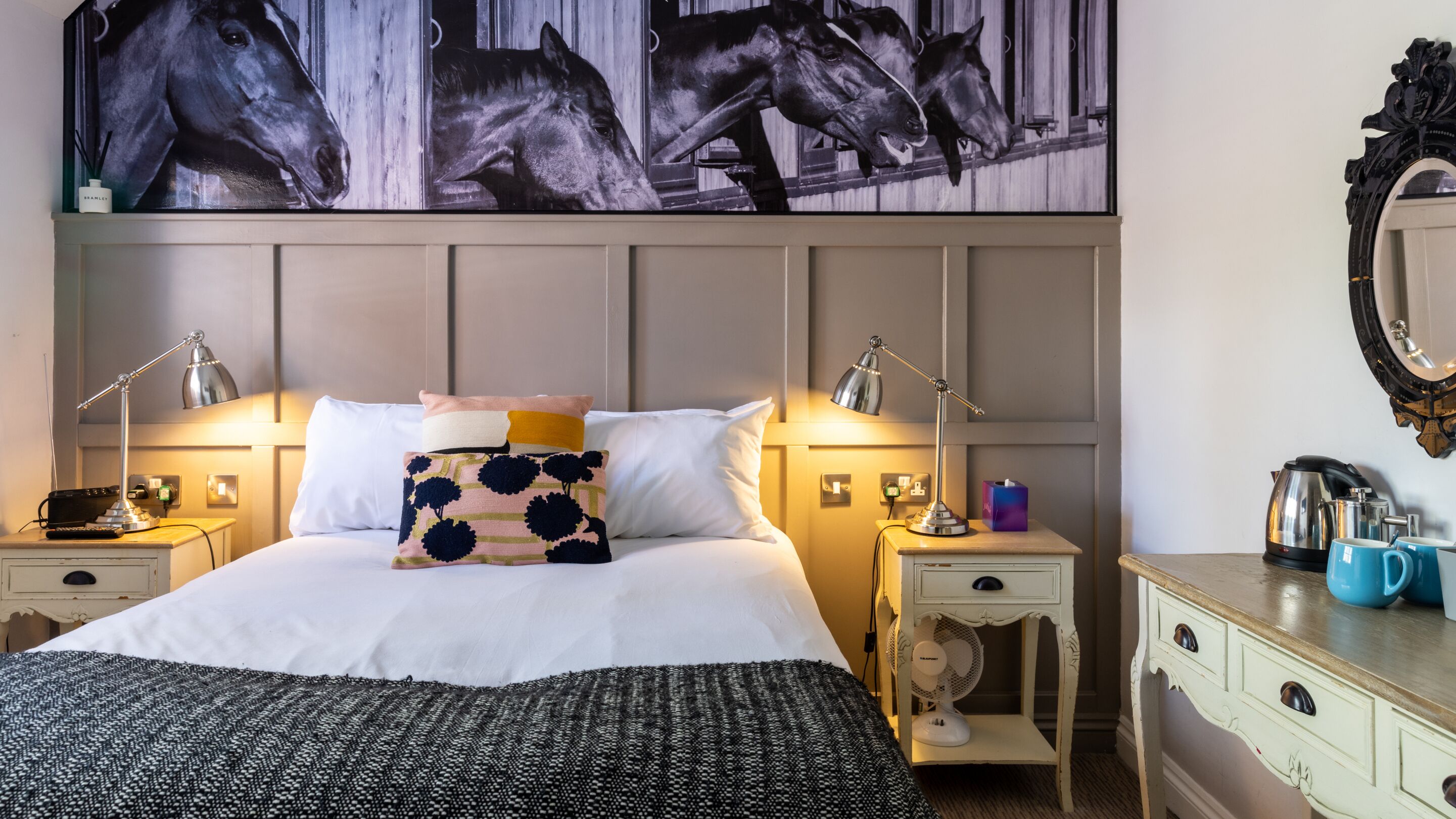 Habitación de hotel con una cama grande, dos mesitas de noche, un tocador, un espejo y una obra de arte colgada en la pared.
