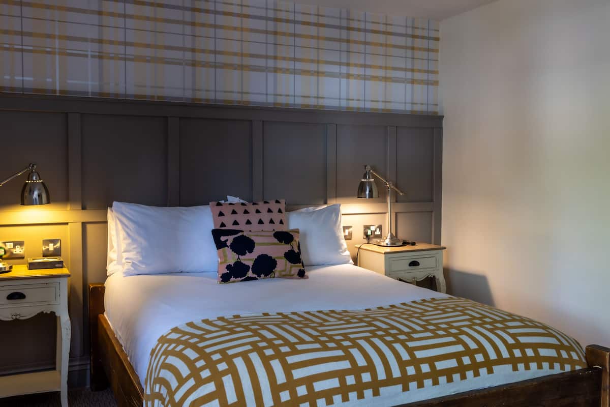 A neatly made bed with a patterned bedspread, two bedside lamps, and a headboard with a checkered design.