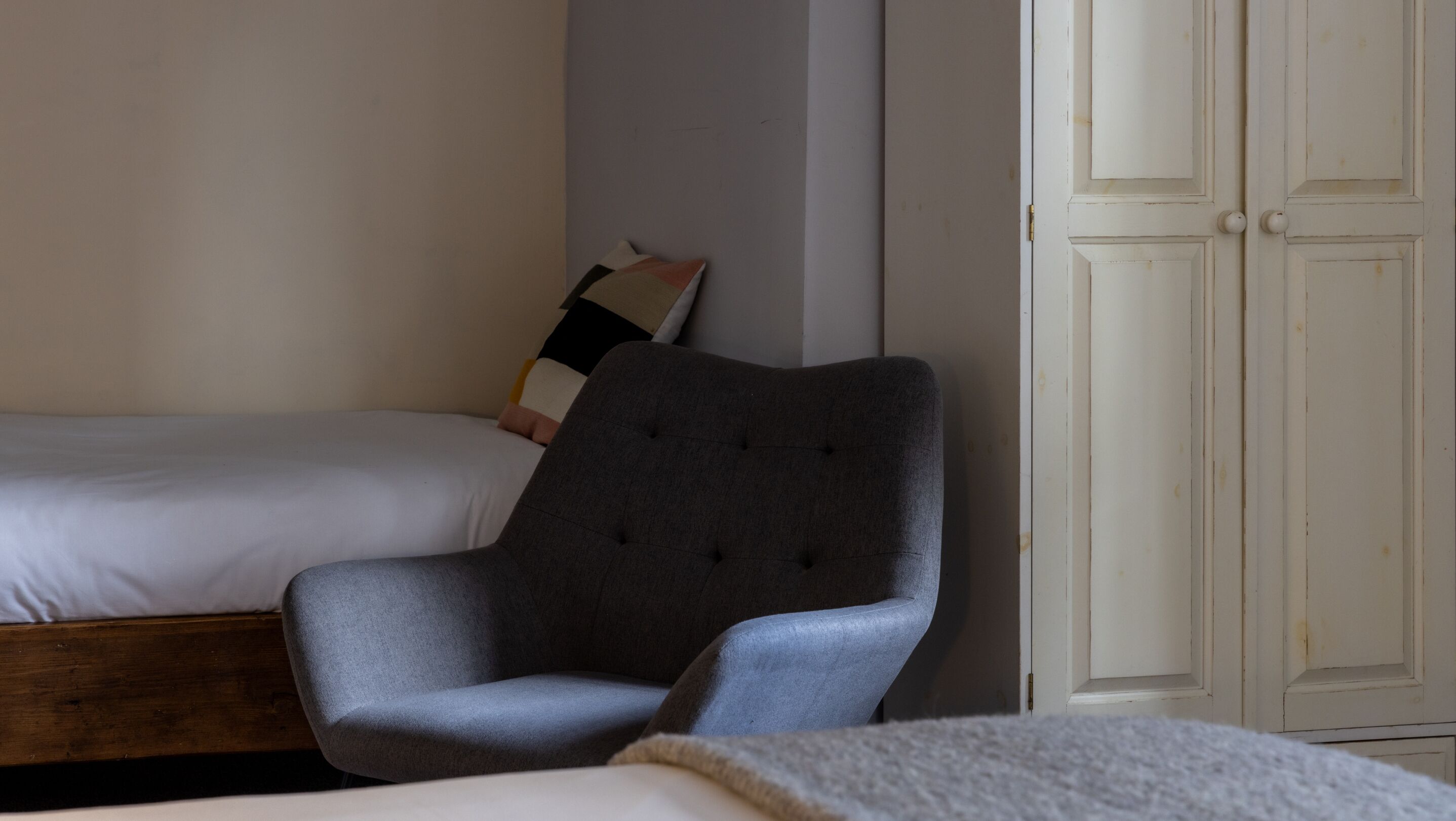 Una camera da letto con un letto, una poltrona grigia imbottita e un armadio bianco.