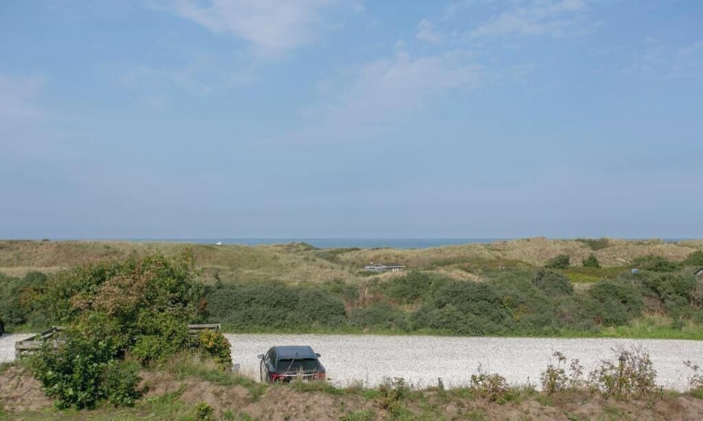 A coastal landscape with a gravel path, a parked vehicle, and vegetation.