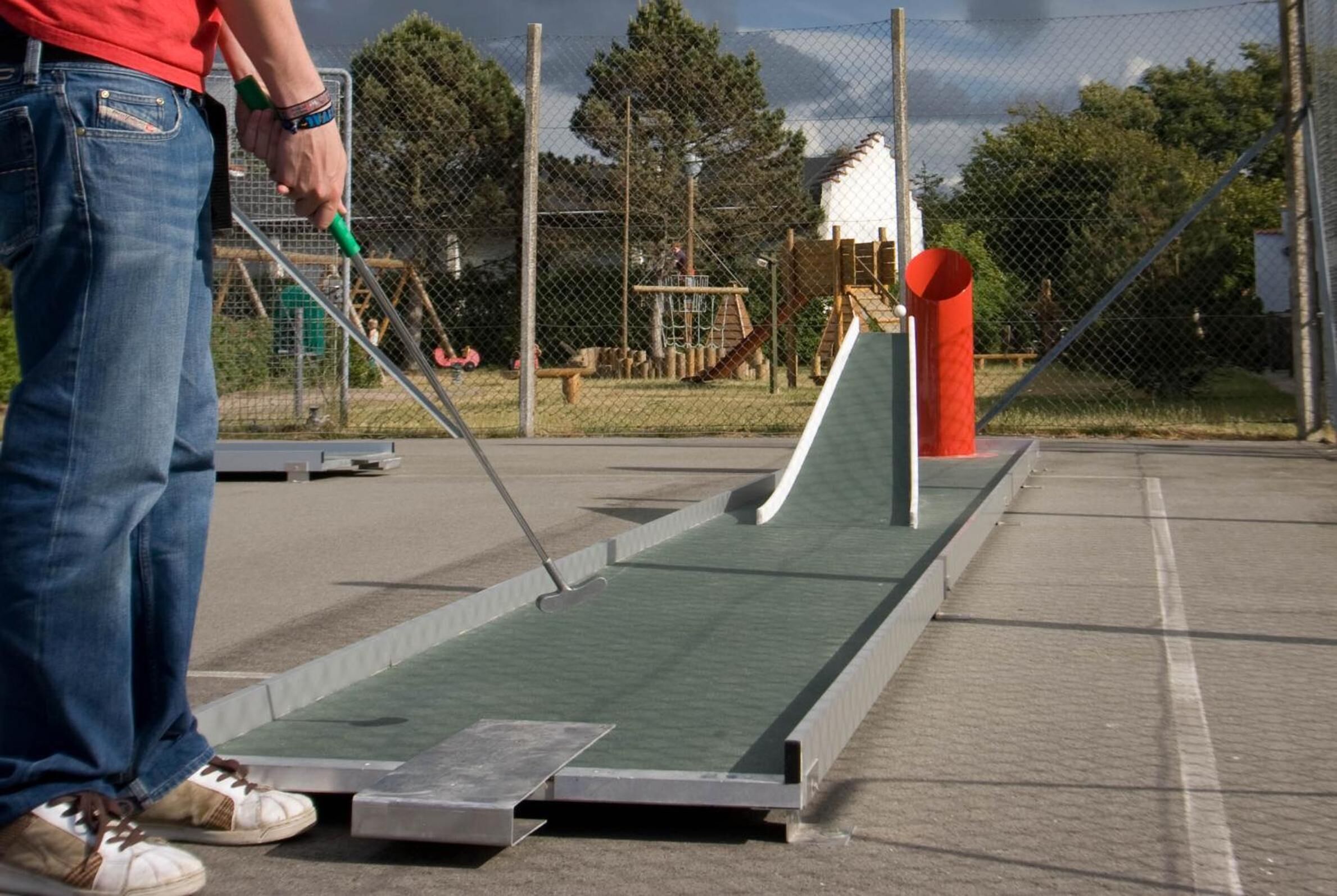 A person standing next to a green ramp with a metal frame, a wooden structure in the background, and a fenced area.