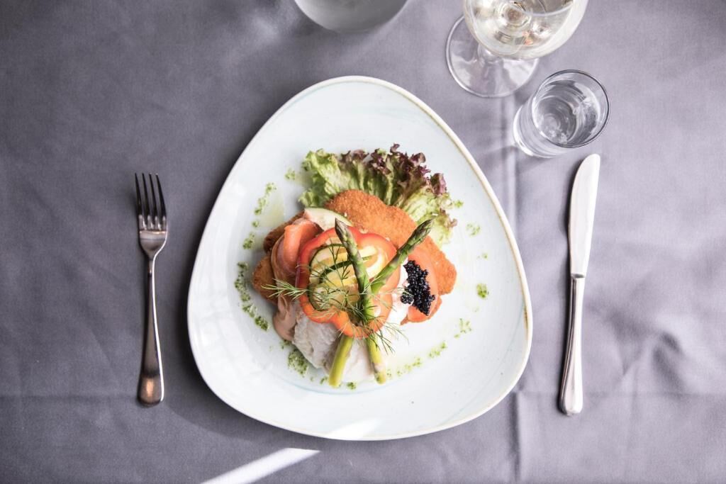 A white plate with a salad, a fork, a knife, and a glass of water on a grey tablecloth.