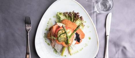 A white plate with a salad, a fork, a knife, and a glass of water on a grey tablecloth.
