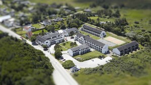 Vista aérea de una zona residencial con varias casas, un edificio grande de techo plano y un campo deportivo.