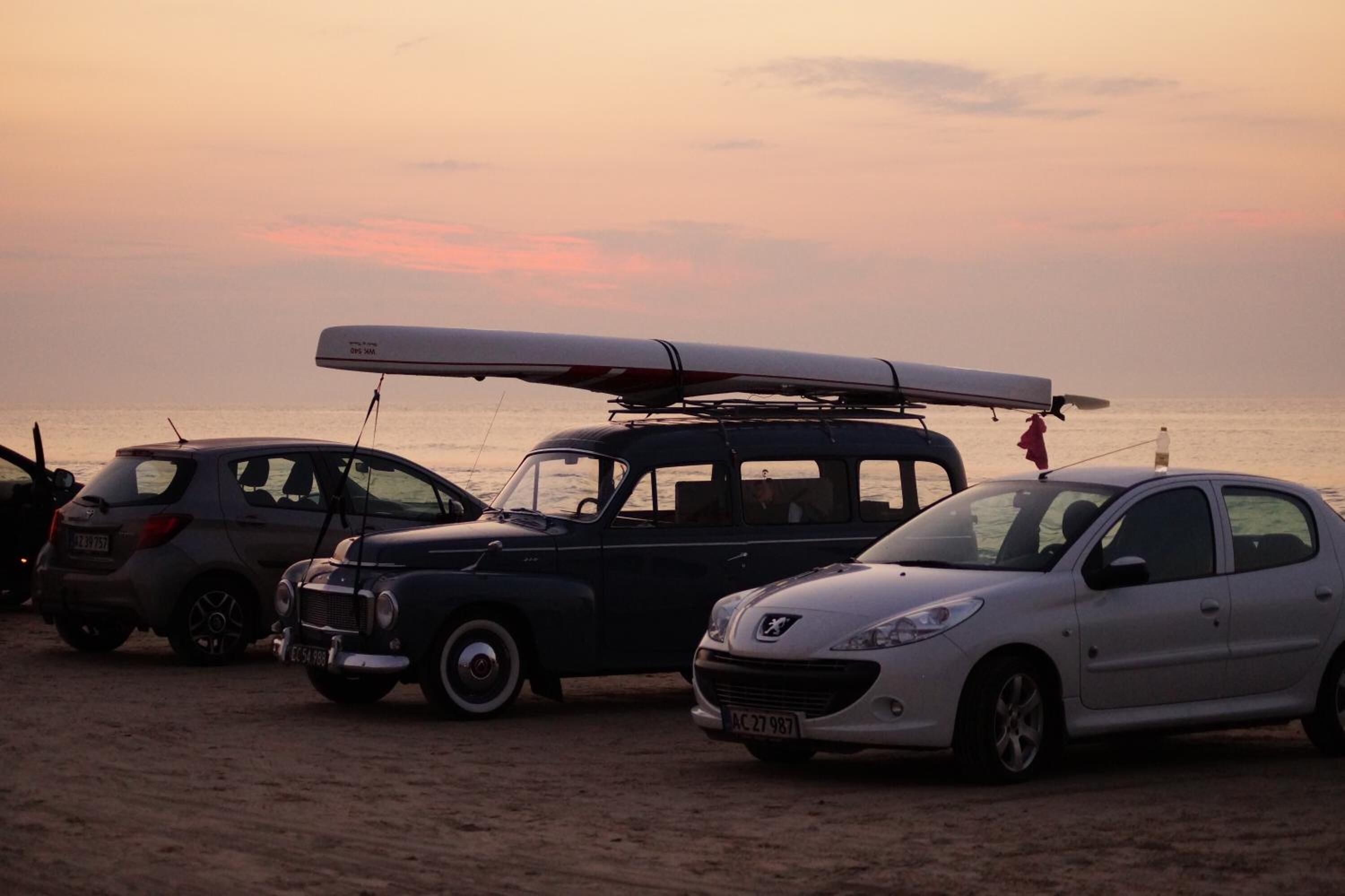 A row of parked cars on a beach at sunset.