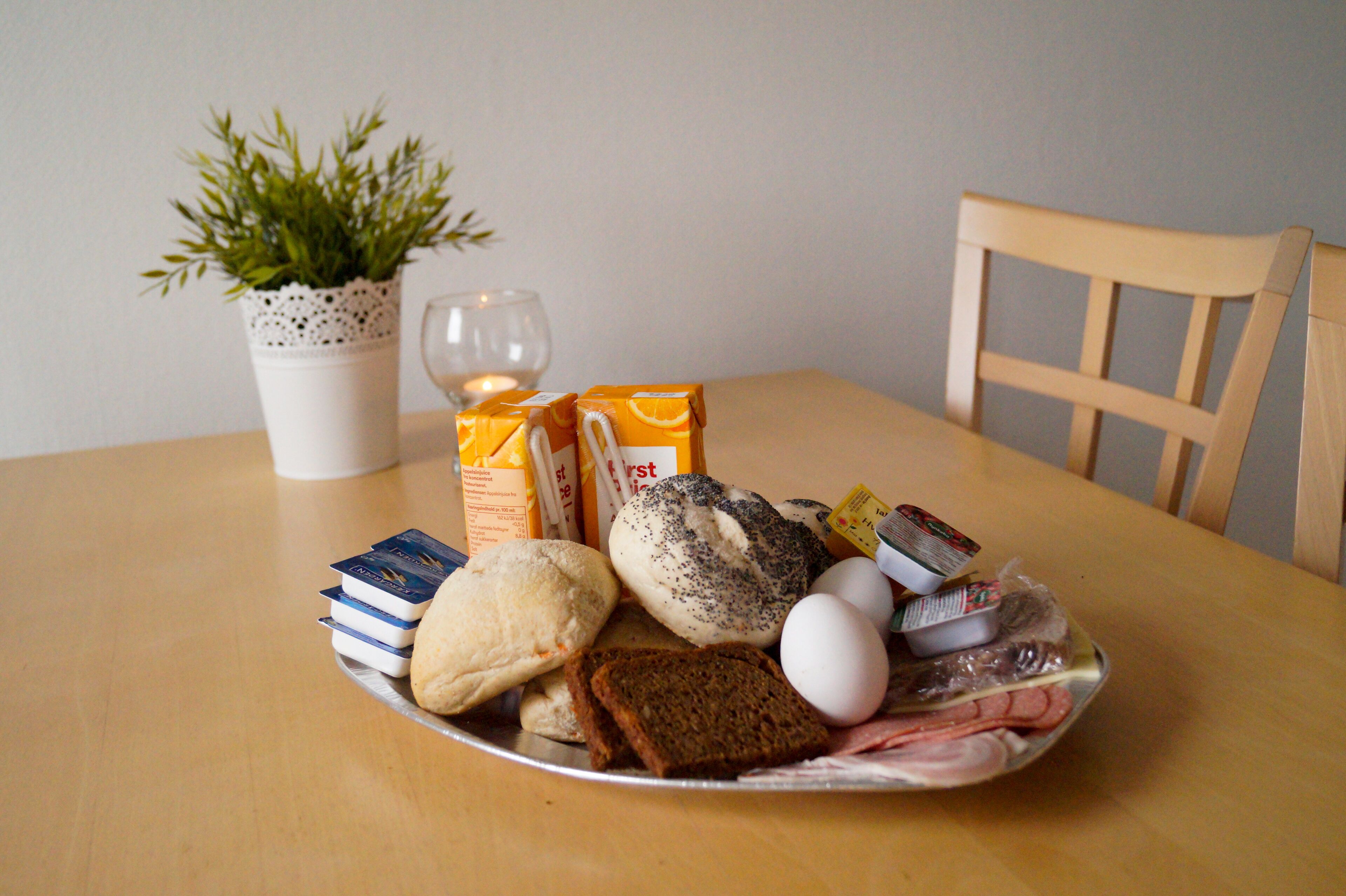 A plate of food including bread, eggs, and butter on a table with a candle and a potted plant.