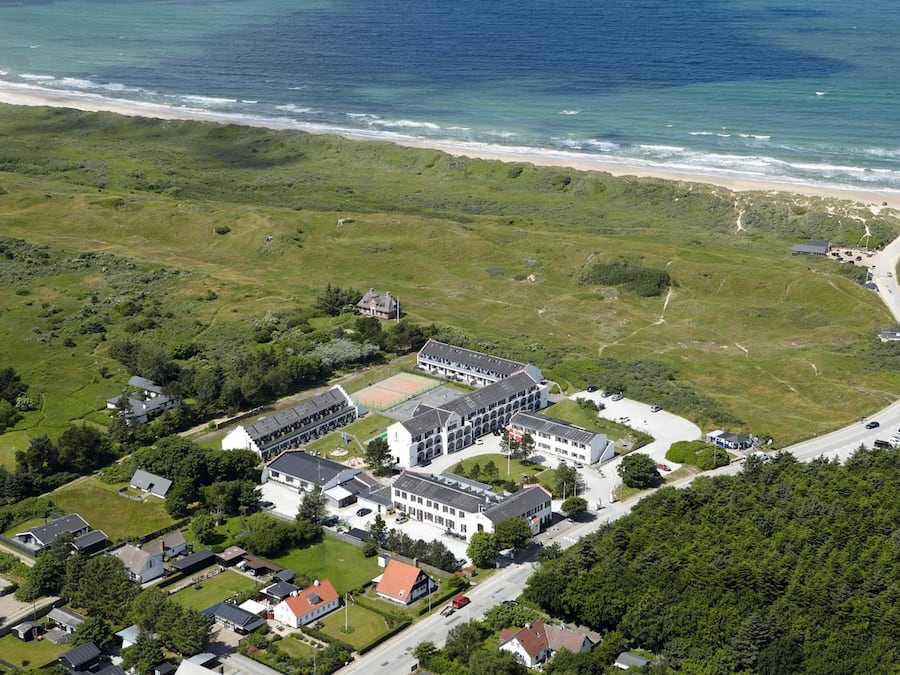An aerial view of a coastal property with a large building complex, a beach, and a winding road.