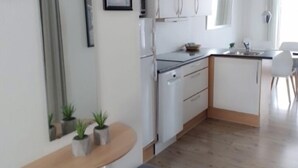 Una cocina moderna con gabinetes blancos, horno empotrado y un lavamanos. Hay un banco con cojín y plantas en macetas sobre una encimera de madera.