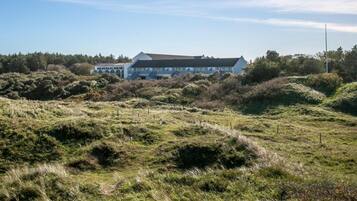 A building with a flat roof and multiple windows, surrounded by a natural landscape with undulating terrain and sparse vegetation.