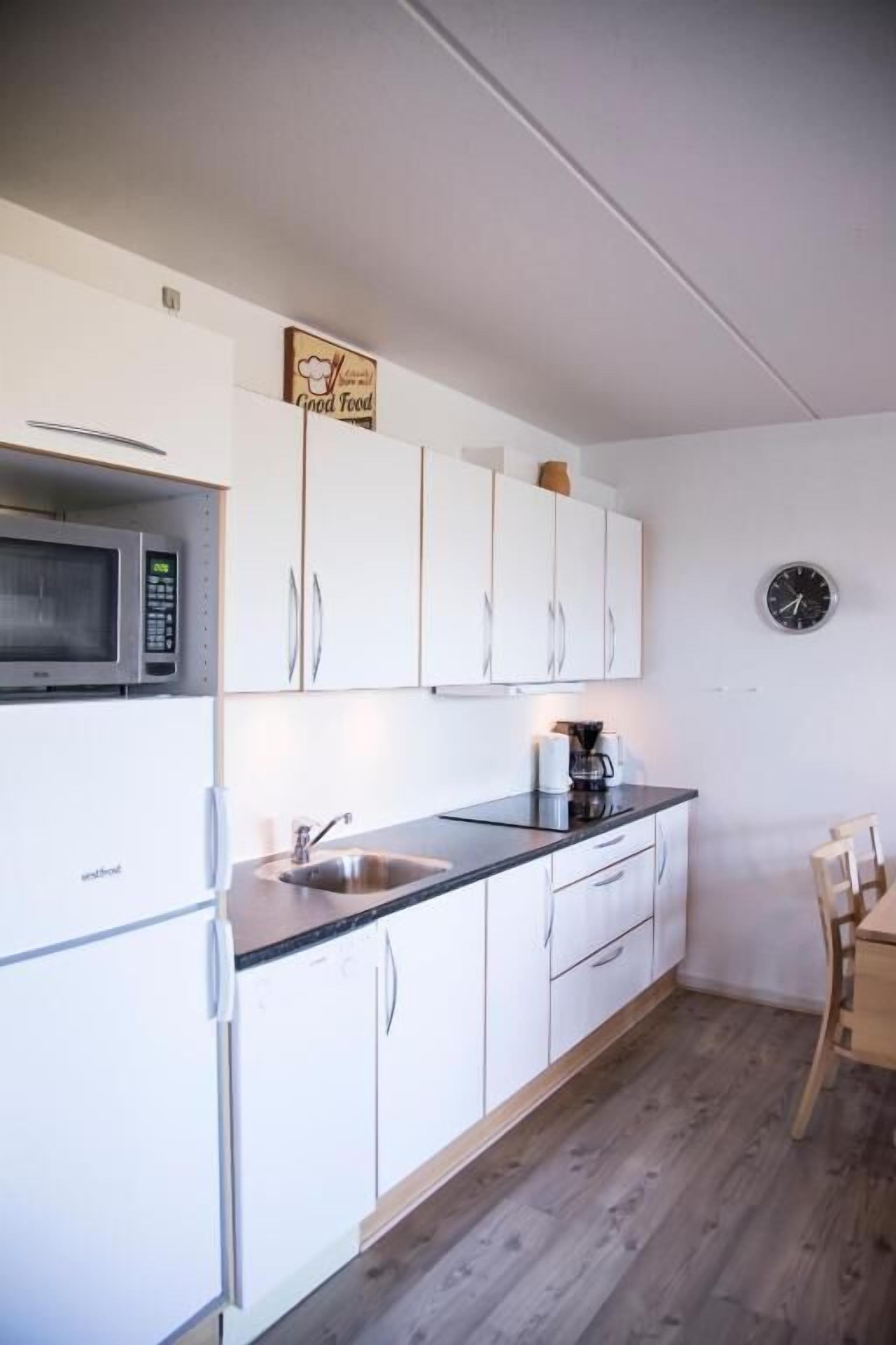 Una cucina moderna con mobili bianchi, un forno a microonde, un lavello e una sveglia a parete.