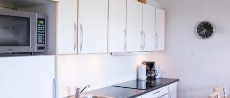 Una cocina moderna con armarios blancos, un microondas, un lavamanos y un reloj en la pared.