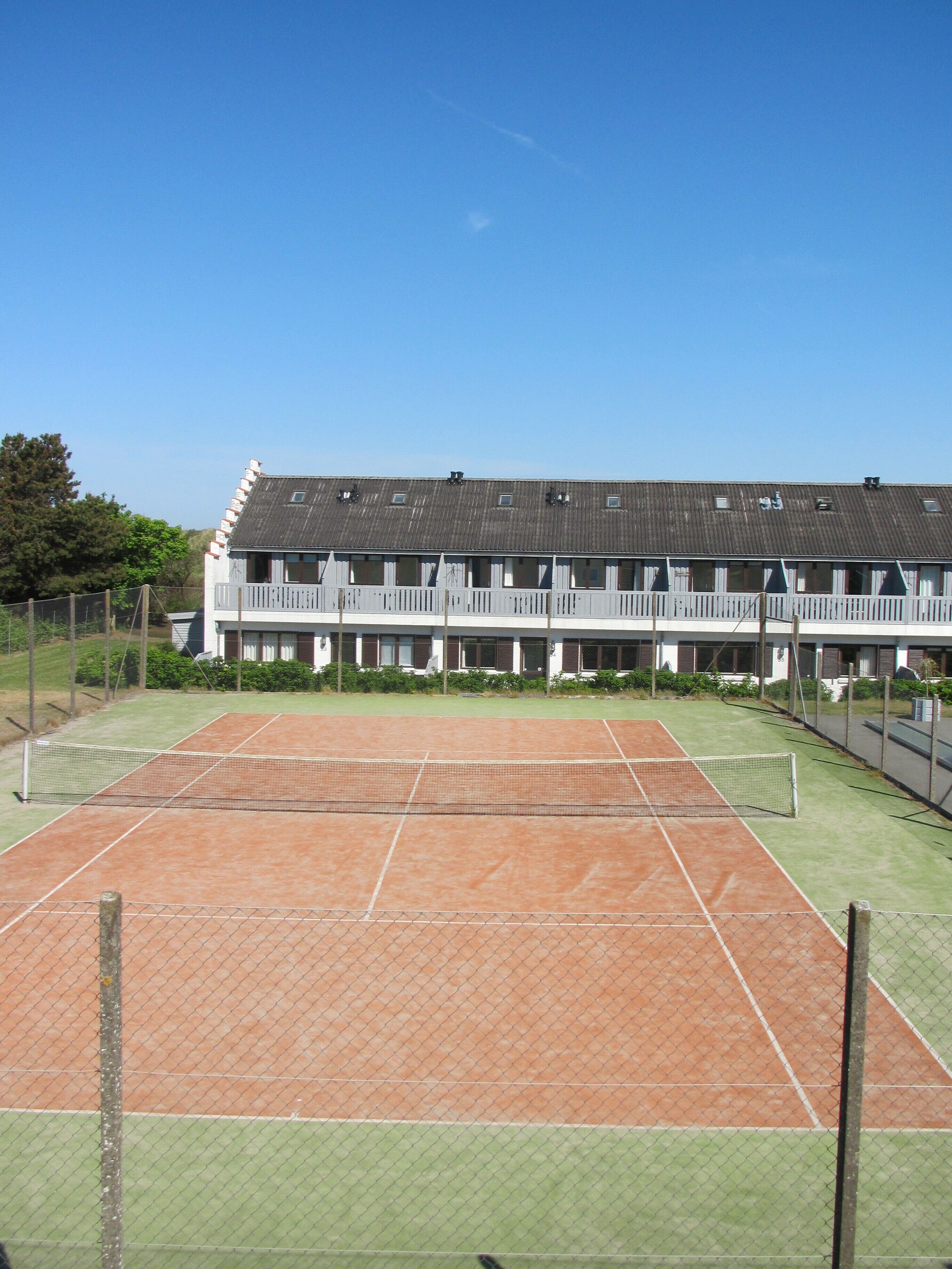 Una cancha de tenis con una red, rodeada por una valla.