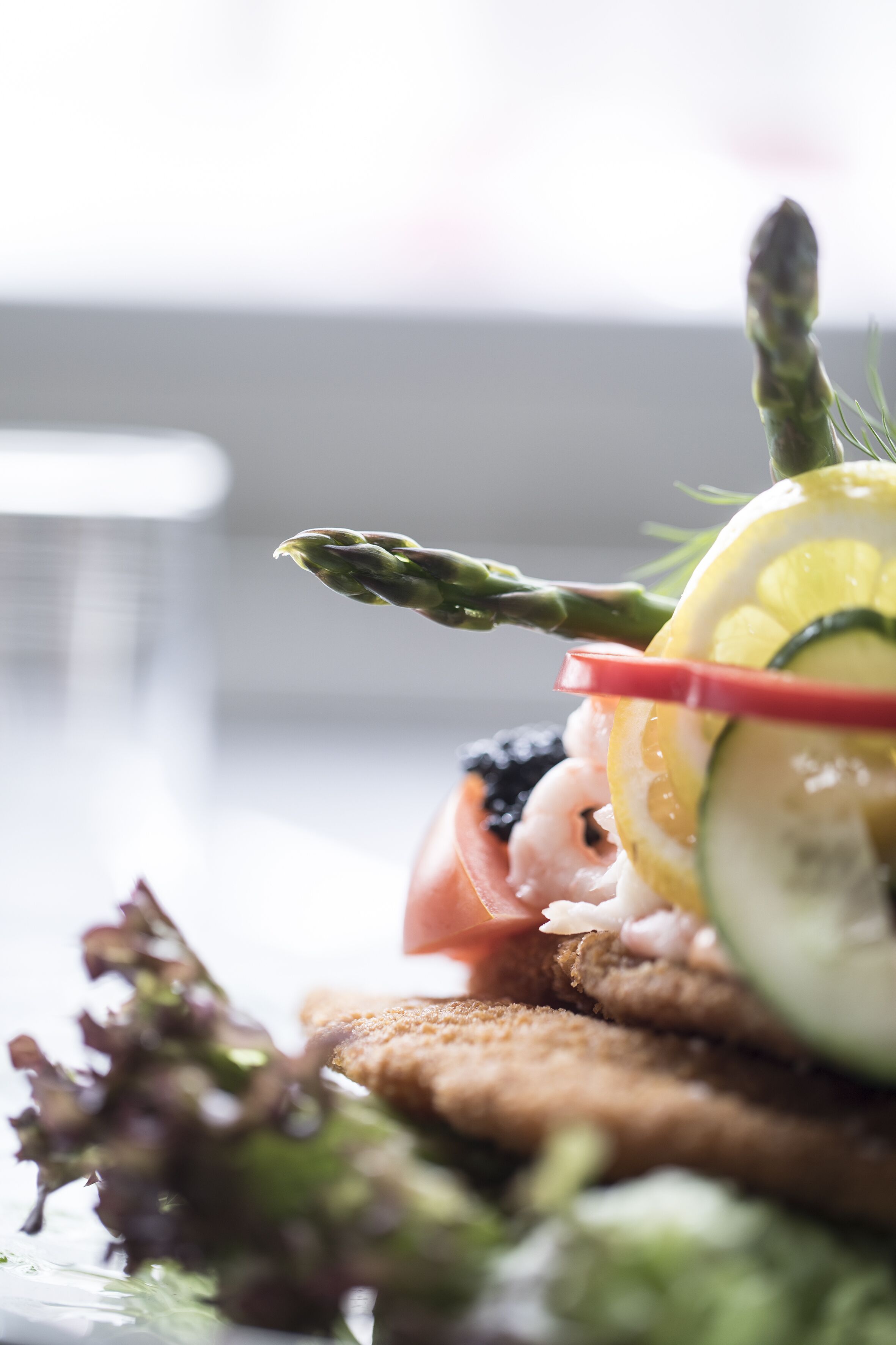 Une vue rapprochée d’une assiette dressée, avec des asperges, des tranches de citron et une garniture de crevettes.