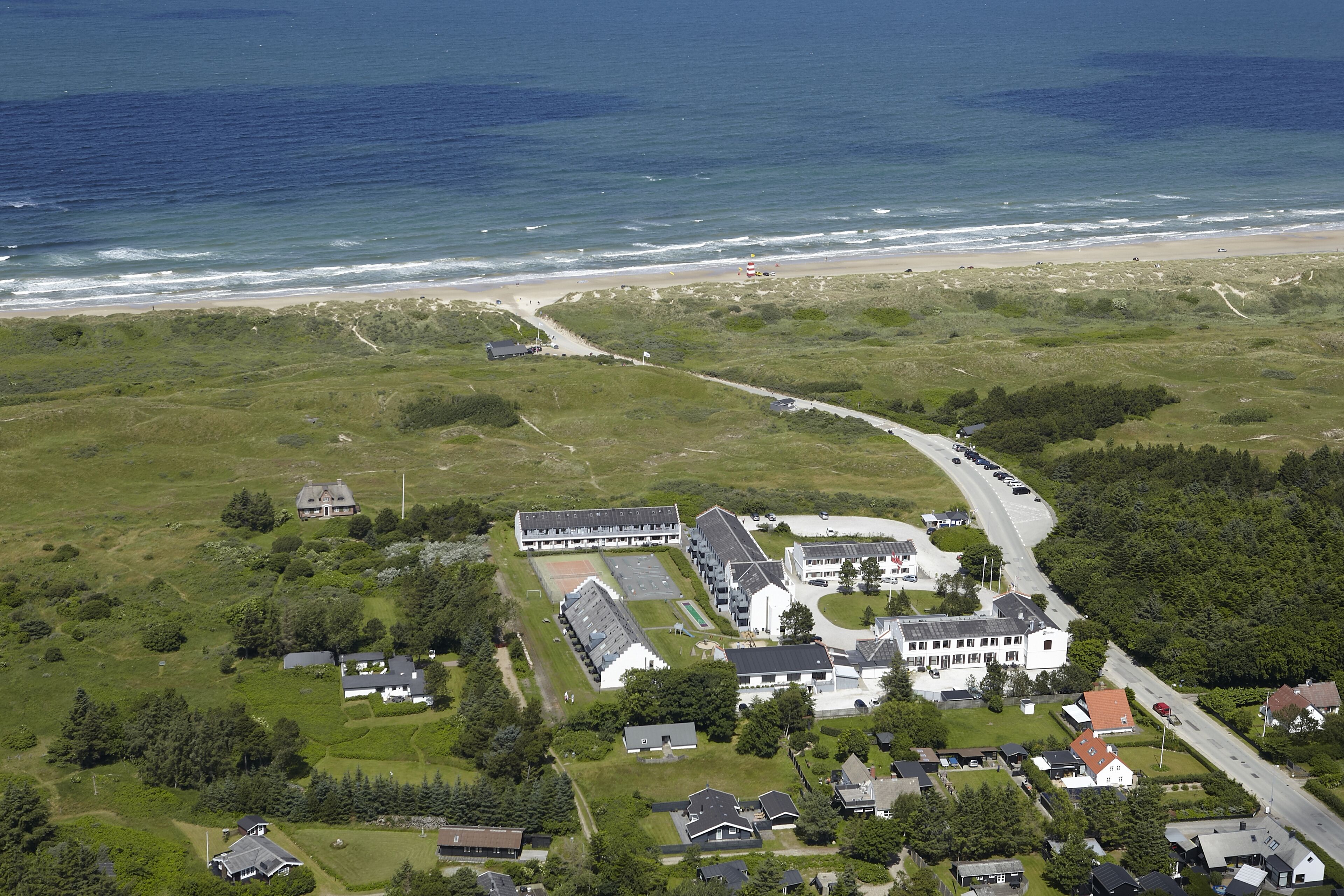An aerial view of a coastal property with a main building, smaller structures, and a road leading to the beach.