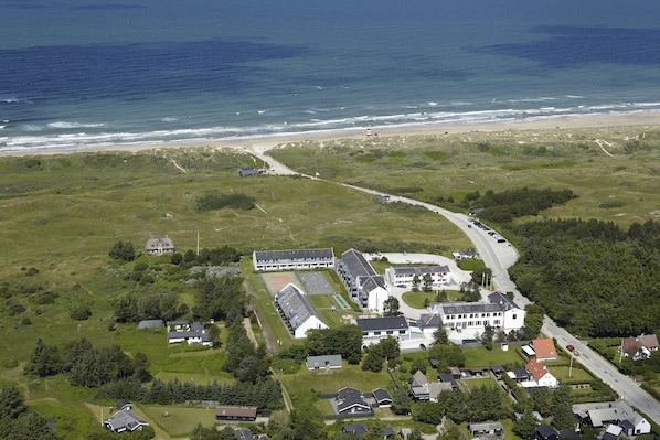 Vista aérea de una propiedad costera con un edificio principal, construcciones más pequeñas y un camino que lleva a la playa.