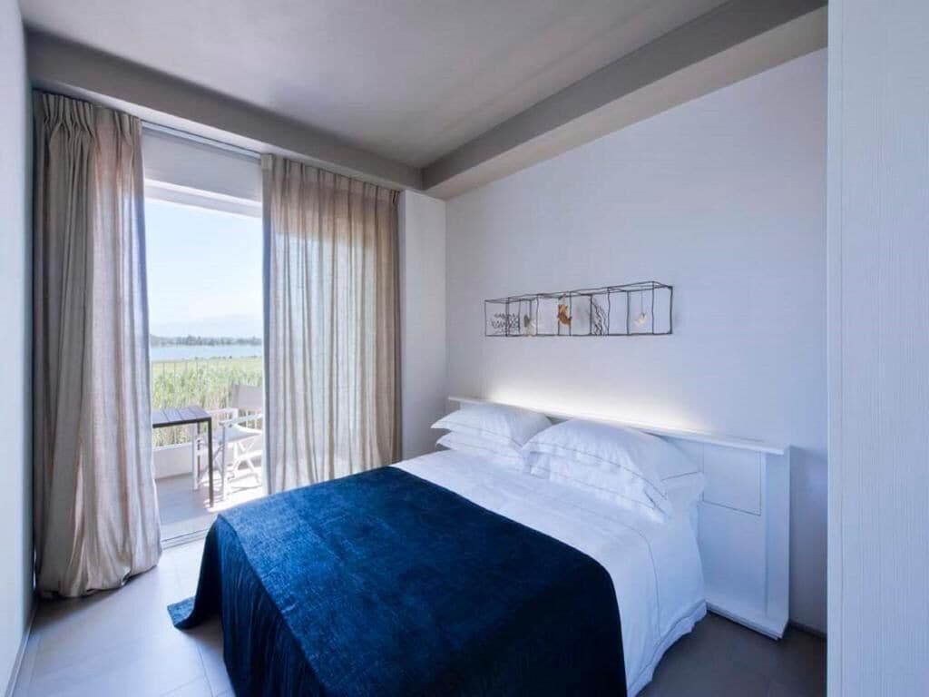 A modern hotel room with a large bed, a balcony with curtains, and a wall-mounted artwork.