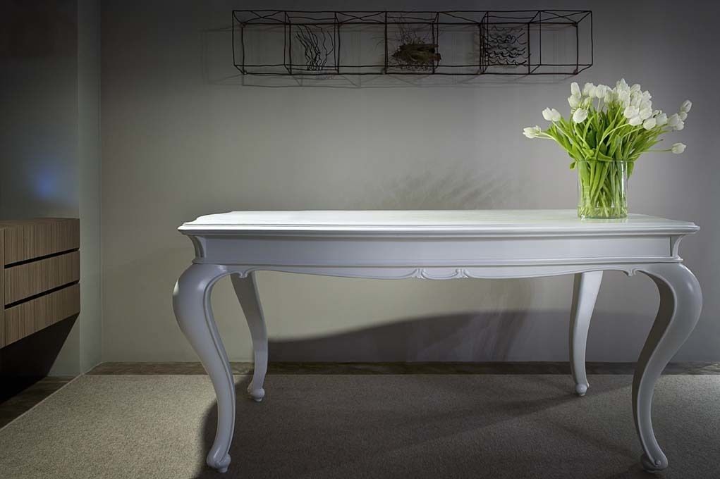 Una mesa blanca con un jarrón de flores blancas sobre un piso alfombrado.