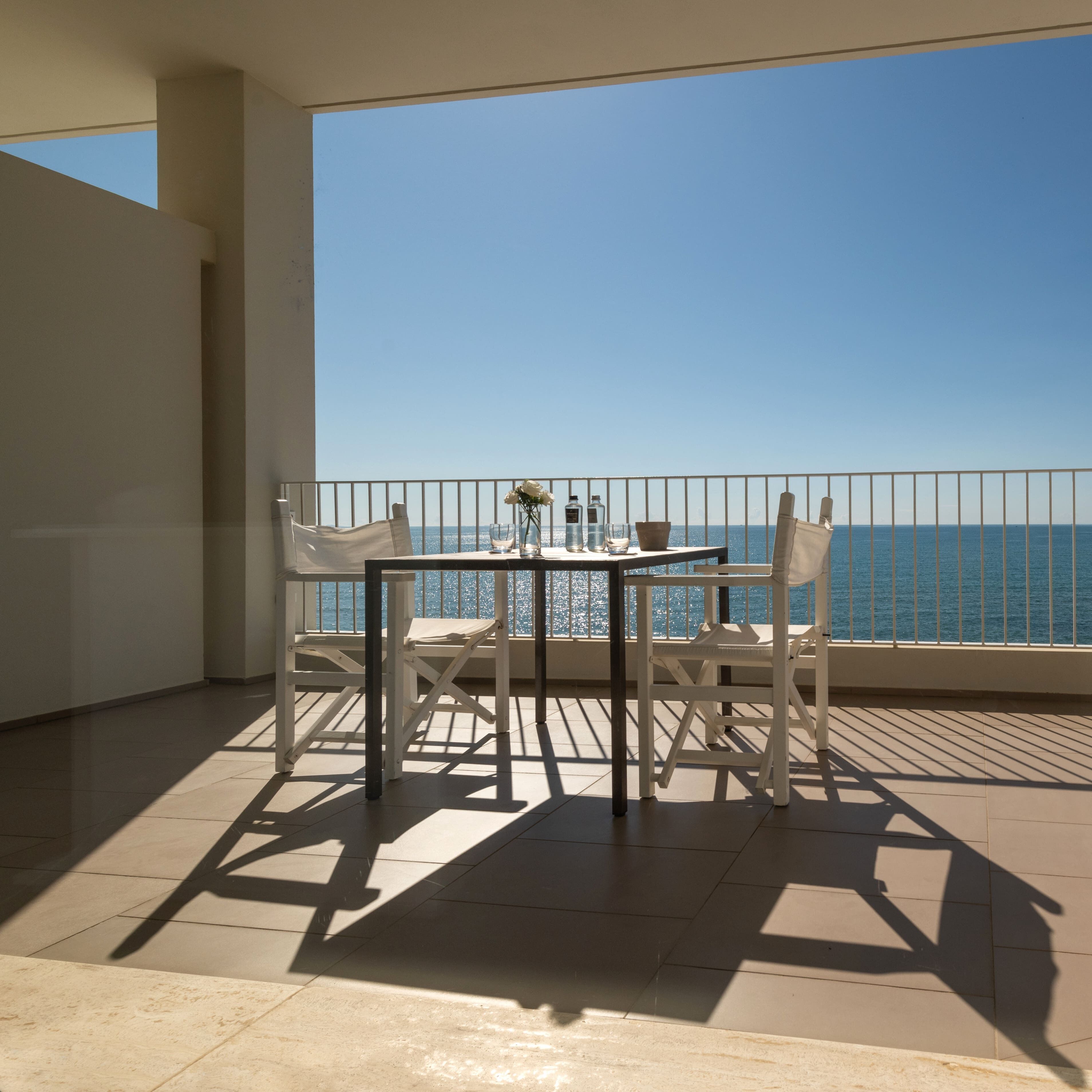 Un balcón con mesa y sillas, barandilla y vista al mar.
