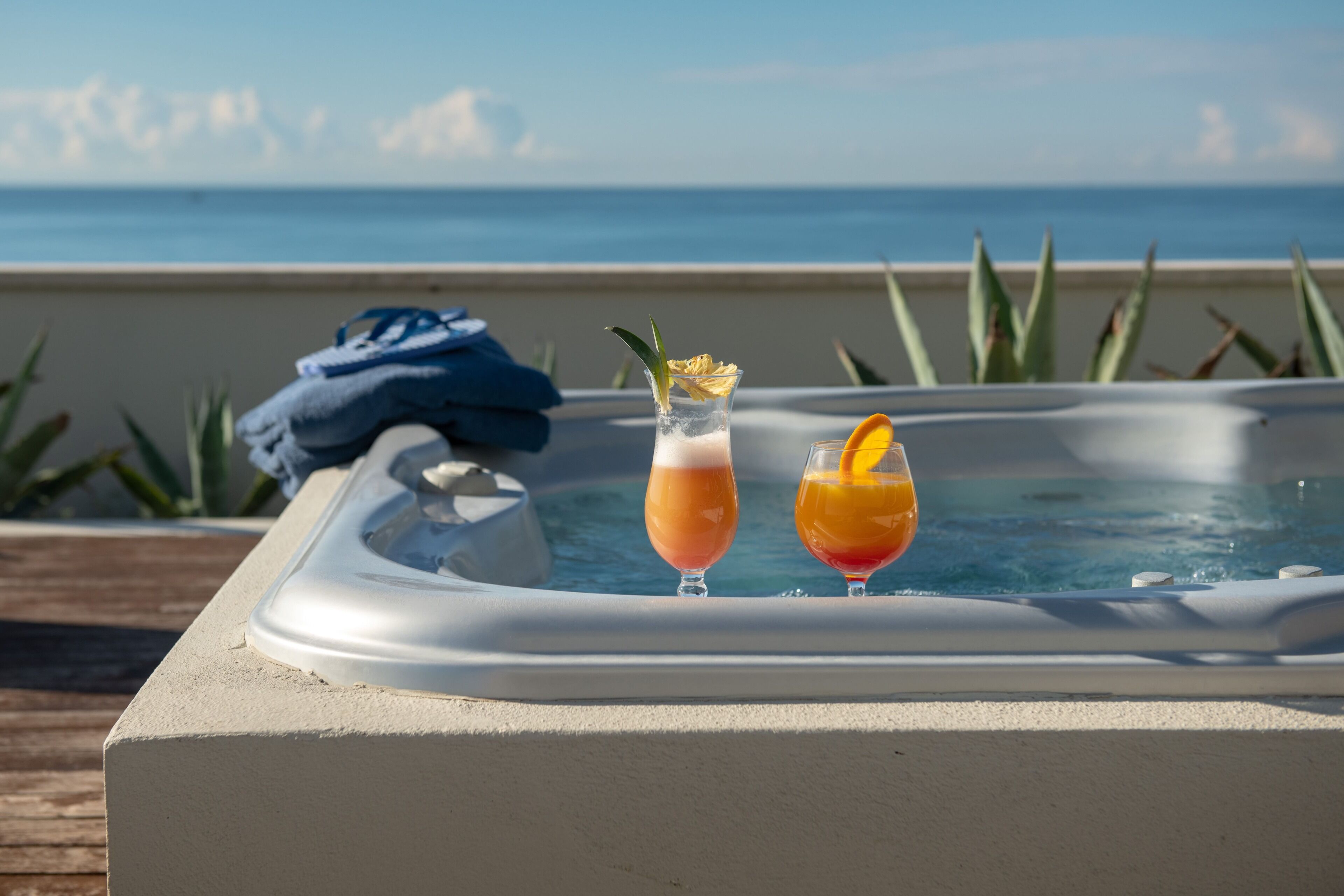 Un bain à remous avec deux boissons, une serviette et une vue sur l’océan.