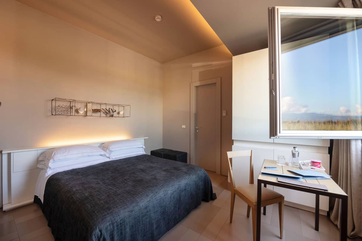 A bedroom with a bed, a desk, and a large window.