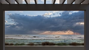 Vista a través de una ventana de una playa con olas y un cielo nublado.