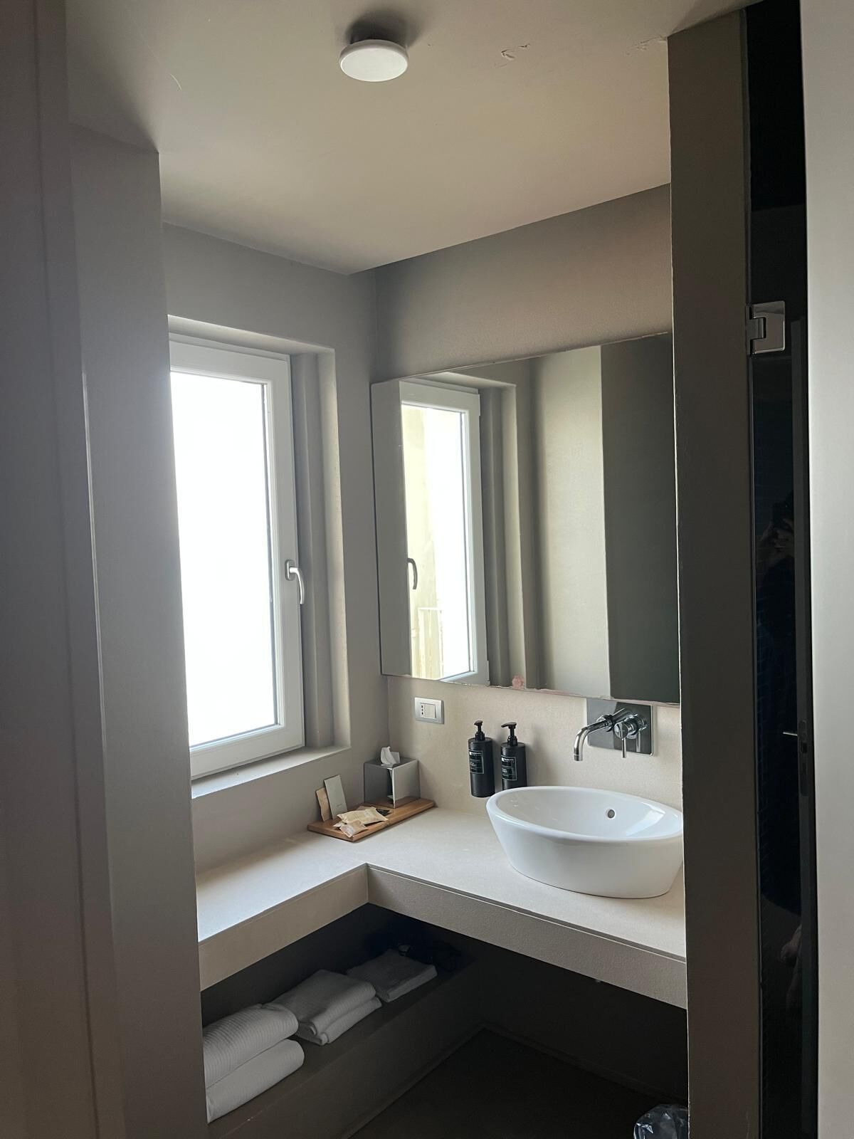 A modern bathroom with a large window, a white sink, and a mirror.