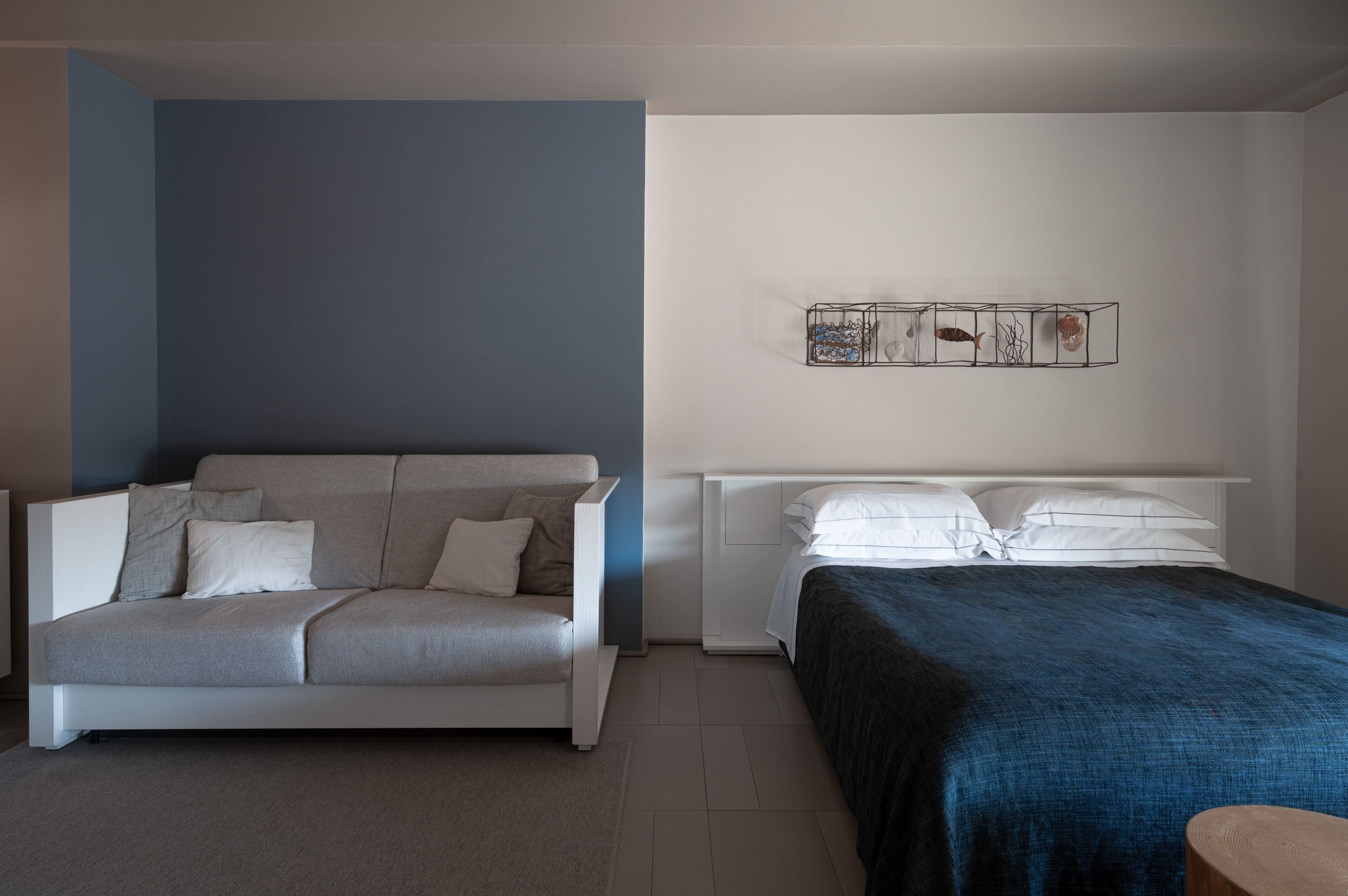 A modern bedroom with a sofa, a bed, a nightstand, and a wall-mounted artwork.