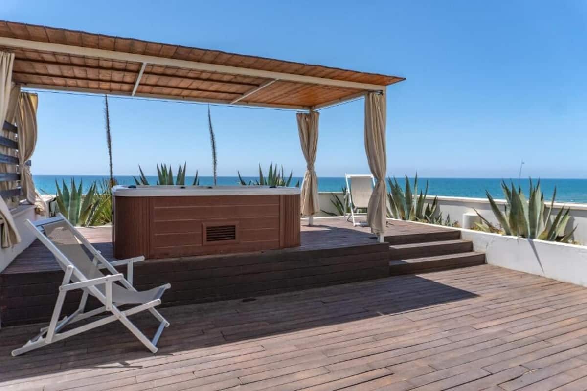 A wooden deck with a hot tub, a covered seating area, and a view of the ocean.