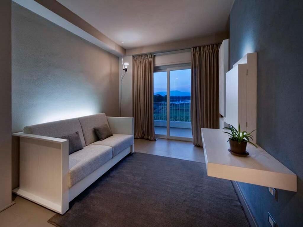 Una habitación de hotel moderna con un sofá, una mesita con una planta, una puerta corrediza de vidrio a un balcón y un aplique de pared.