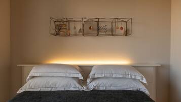 Una cama con almohadas blancas y una manta oscura, una mesita de noche y una lámpara fijada a la pared.