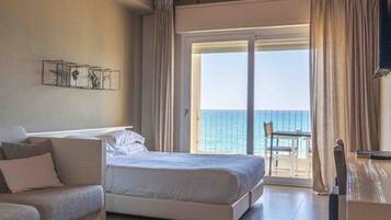 Une chambre d’hôtel avec un lit, un canapé, un bureau et une vue sur la mer, visible à travers une grande fenêtre.