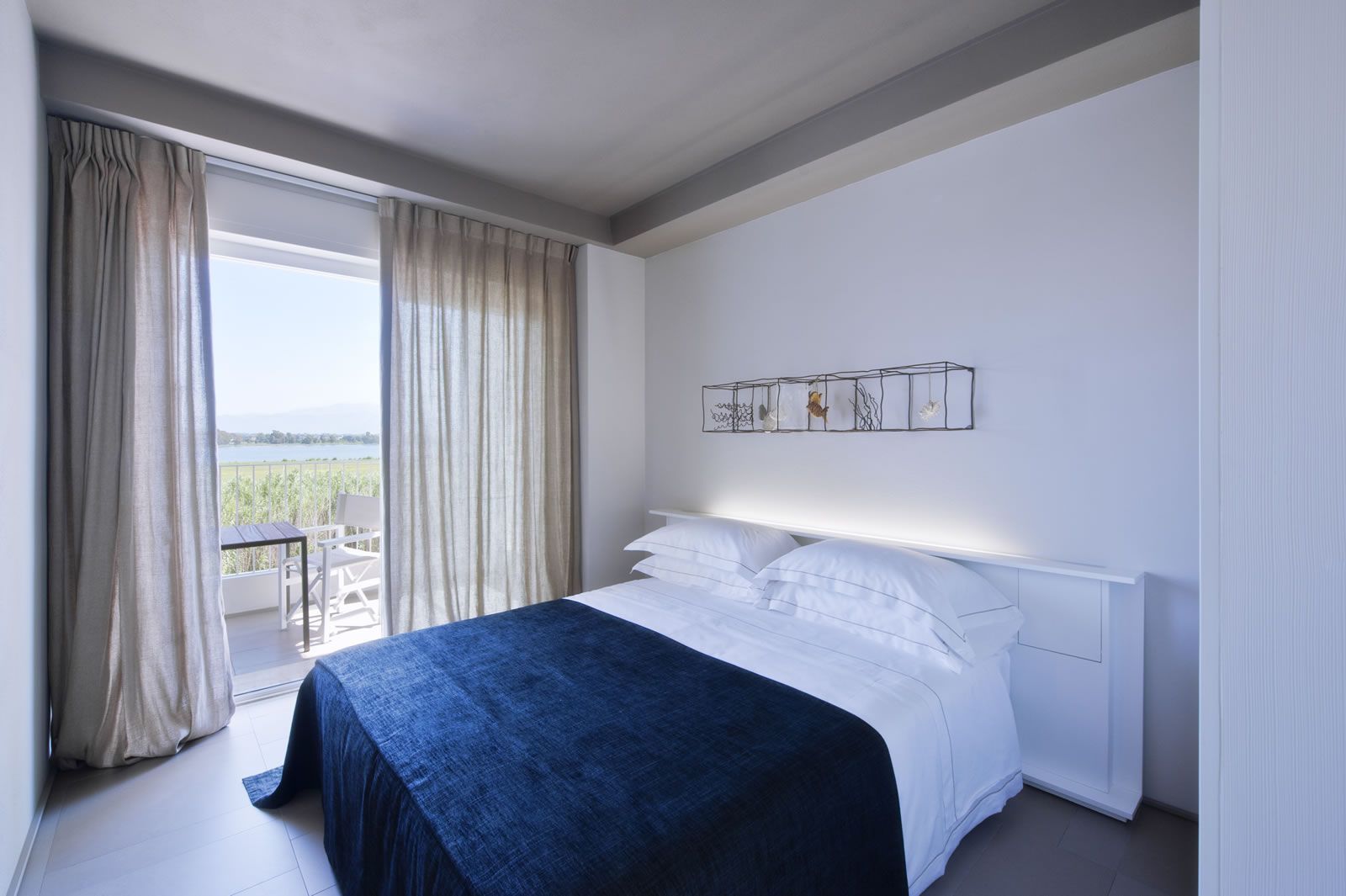 A modern hotel room with a large bed, a balcony with a table and chairs, and a view of the outdoors.