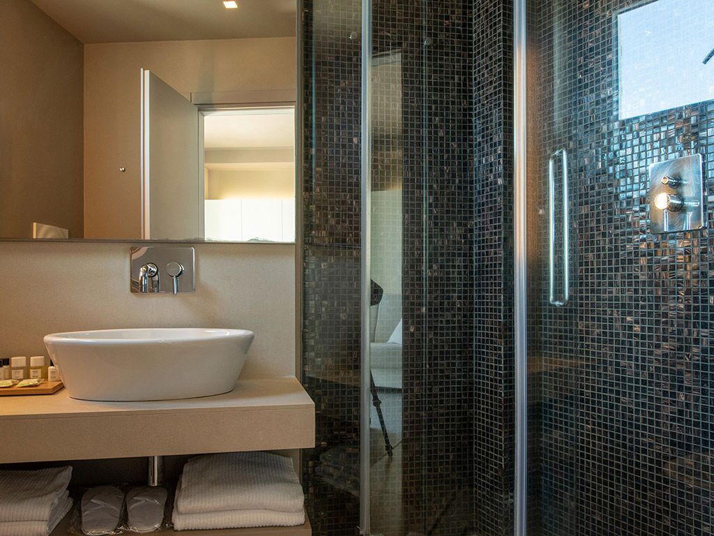 A modern bathroom with a large white sink, a glass shower enclosure, and a mirror above the sink.