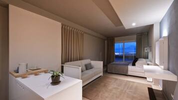 A modern hotel room with a sofa, a bed, a small table with a plant, and a view of the city at dusk.