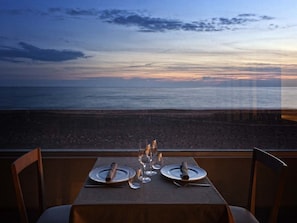 Une table dressée pour deux, avec vue sur la plage et l’océan au coucher du soleil.