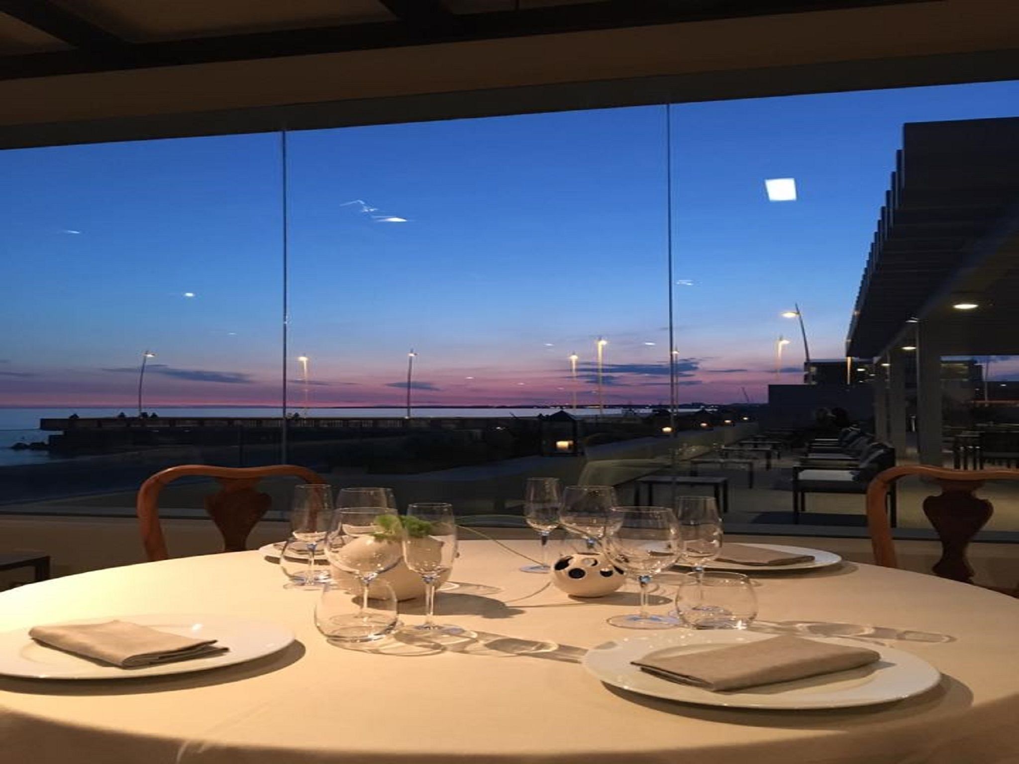 A table set for dining with a view of the sunset over the ocean.