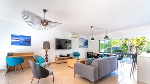 A modern living room with a sofa, chairs, a TV, and artwork on the walls. - Domaine Villas Mandarine (Calvi)