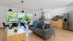 A modern kitchen with a grey sofa, wooden dining table, and black chairs. - Domaine Villas Mandarine (Calvi)