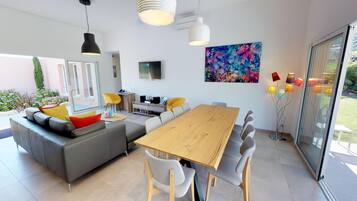A modern living room with a sofa, a wooden dining table, and a TV.