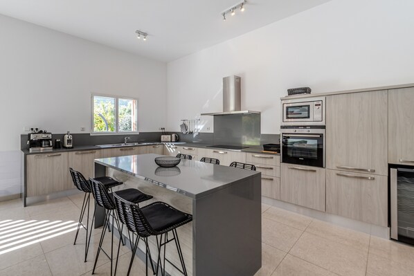 A modern kitchen with a central island, black bar stools, and built-in appliances.