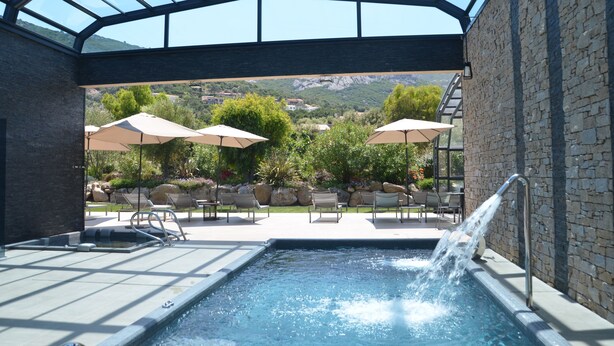 A pool area with a glass ceiling, outdoor seating, and a view of the mountains. - Domaine Villas Mandarine (Calvi)