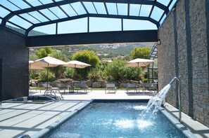 A pool area with a glass ceiling, outdoor seating, and a view of the mountains.