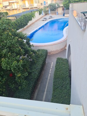 A swimming pool surrounded by greenery, with a paved walkway and a building in the background. - Hotel Alexander (Giardini Naxos)