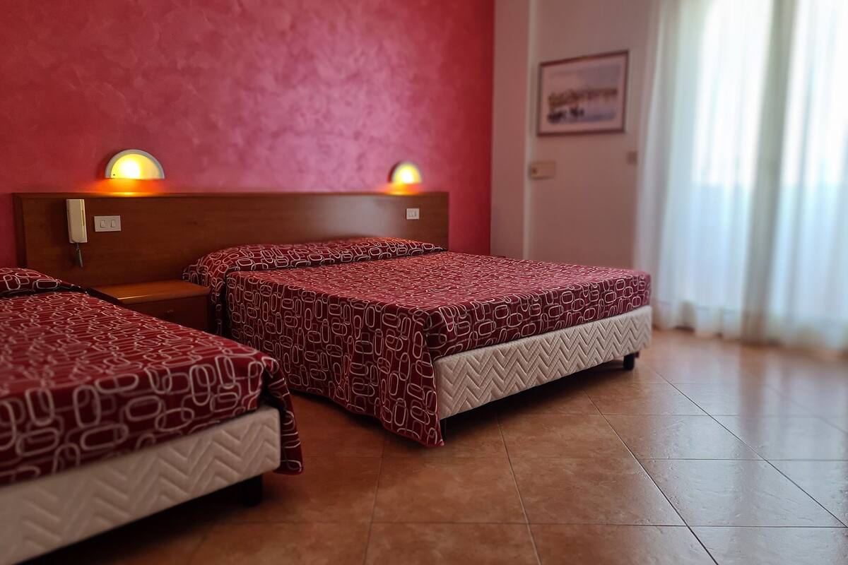 A hotel room with three beds, each with patterned bedding, a wooden headboard, and a wall-mounted phone.